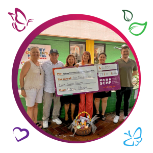 A group of six people is standing in front of a green building, holding a large ceremonial cheque. The cheque is made out to the Sydney Children’s Hospitals Foundation for the amount of $6,800. The date on the cheque is 27/11/2024, and it is from 'COOL MARIE.' The cheque and the people are framed within a circular border with butterfly and leaf graphics. There is also a basket with various items placed on the ground in front of the group.