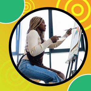 A person with braided hair is painting on a canvas placed on an easel. The person is wearing a light-colored sweater and ripped jeans, and is holding a paintbrush in one hand and a palette in the other. The background features large windows, and the image is framed with a circular border on a colorful background with green and yellow circles.