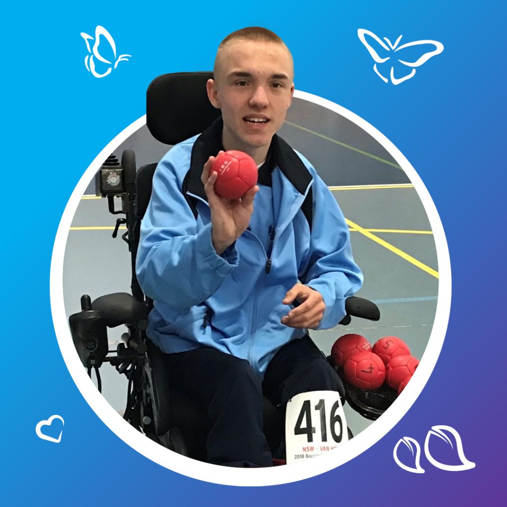 A person in a wheelchair is holding a red ball, poised to throw. They are wearing a blue jacket and dark pants, with several other red balls resting on their lap. The wheelchair displays the number “416.” The setting is a sports court marked with yellow lines, suggesting a game in progress. The image is framed with a blue border, decorated with butterflies and hearts