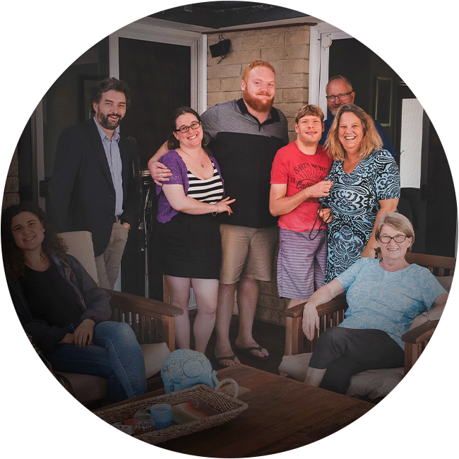 A group of people sitting and standing in and outdoor patio smiling at the camera. the image is in a circle cut out.