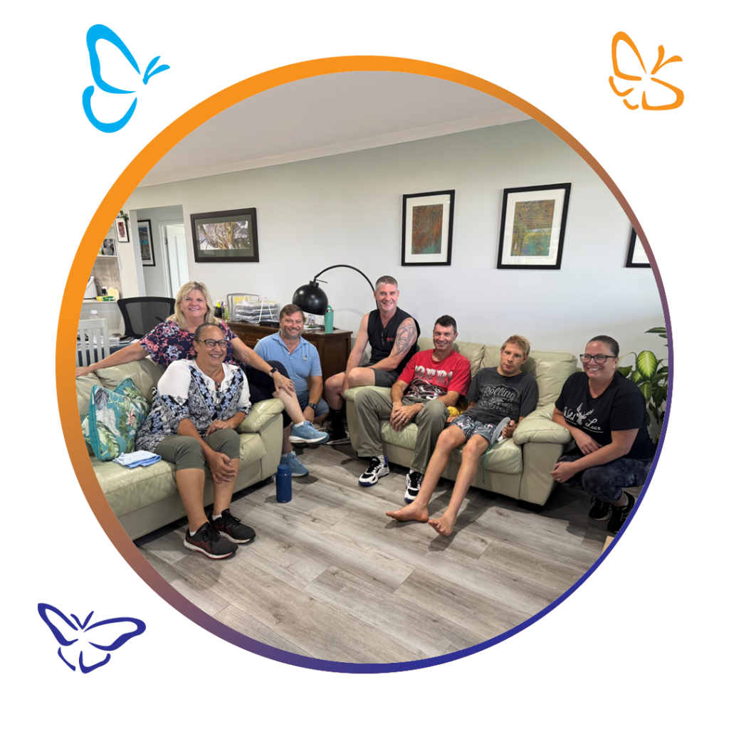 An image of a group of people sitting on lounge chairs in a living room smiling at the camera. the image is inside a circle, with an orange and dark blue boarder with icons of butterflies round the outside of the circle.