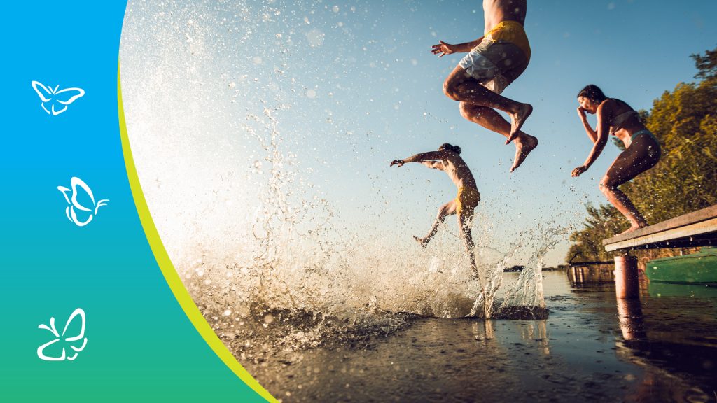 Three people leap off a wooden dock into a sunlit lake, their bodies suspended mid-air as water splashes dramatically below. Their playful poses radiate joy and freedom, set against a backdrop of trees and a clear blue sky. On the left, a vertical strip with a blue-to-green gradient features three white butterfly icons, adding a whimsical, nature-inspired accent to the scene.