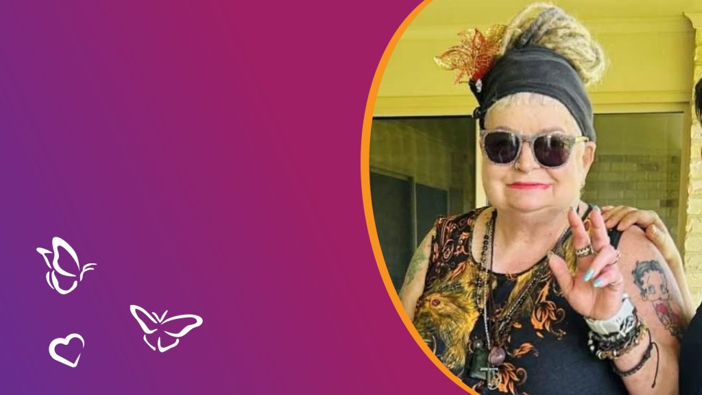 An older person with light hair in a headscarf and sunglasses smiles and gestures with one hand. They wear a patterned sleeveless top and jewelry, framed by a purple background with butterfly and heart icons.