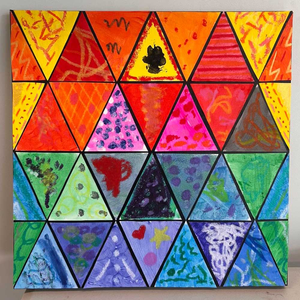A vibrant abstract painting composed of twenty-one equilateral triangles arranged in three rows and seven columns. Each triangle is outlined in black and filled with unique colors and patterns, ranging from warm reds, oranges, and yellows at the top to cool greens, blues, and purples at the bottom. The designs include dots, zigzags, brushstrokes, and small shapes such as a black blotch, a red cup, a heart, and a yellow star. The artwork blends geometric structure with expressive, playful creativity.